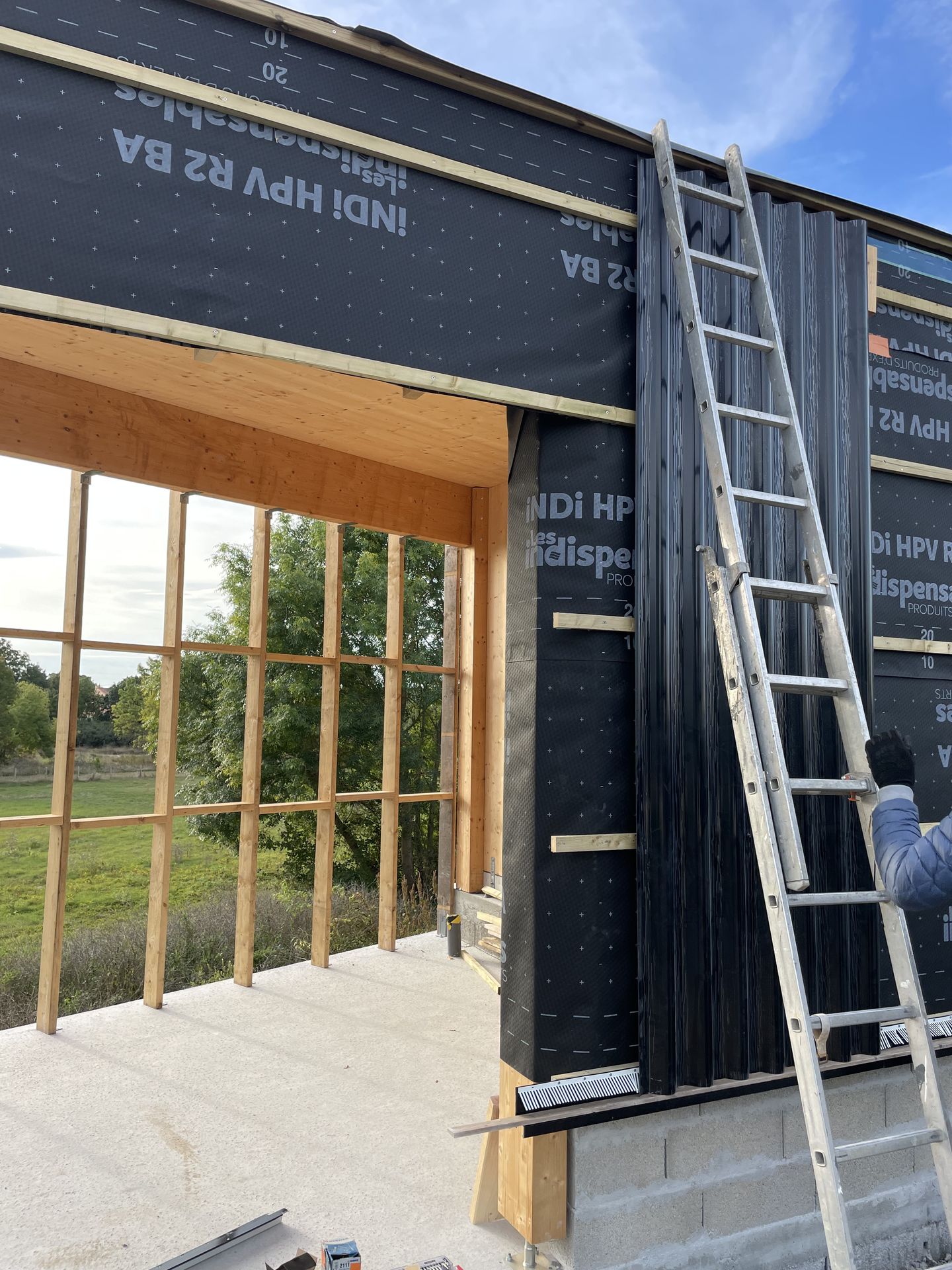 Photo de la pose du premier panneau du bardage en taule ondulée de la maison Le Triangle